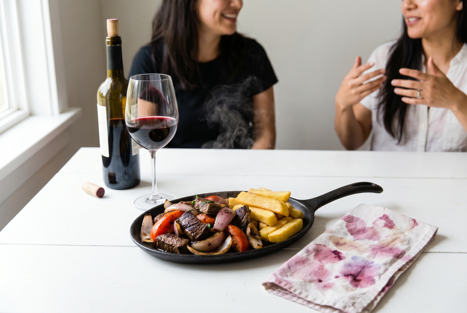 Plato de lomo saltado peruano servido junto a una copa de vino tinto sobre una mesa luminosa